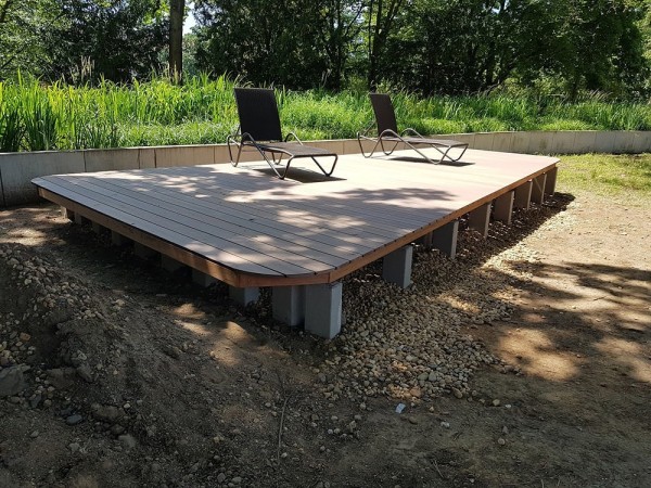 Ein Sonnendeck aus Holz in einem frisch umgegrabenen Garten. Darauf stehen zwei Liegestühle.