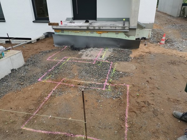 Eine Gartenbaustelle. Auf der braunen Erde sind mit pinker und gelber Farbe Quadrate als Markierungen eingezeichnet.
