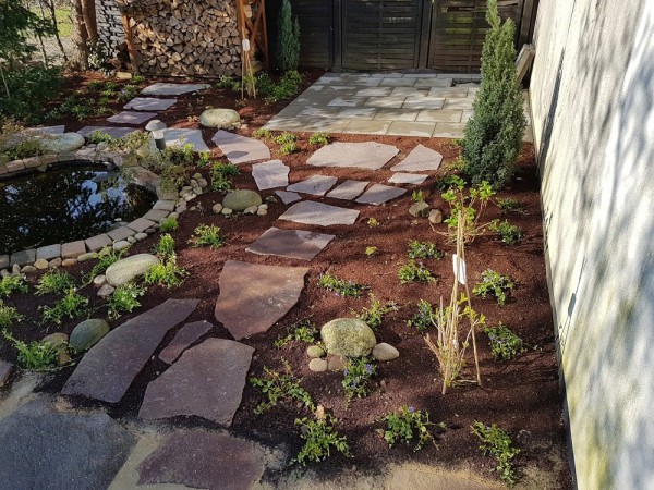Draufsicht auf einen Garten. In der Mitte ein Weg auf großen unebenen Steinplatten, links ein mit Steinen umringter Teich und rechts ein frisch bepflanztes Beet.