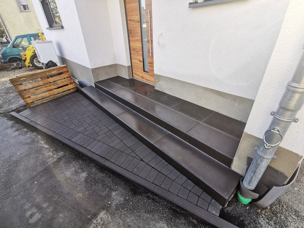 Ein Hauseinangang der aus verschiedenen Steinbodenplatten assymetrische Treppenstufen aufweist.