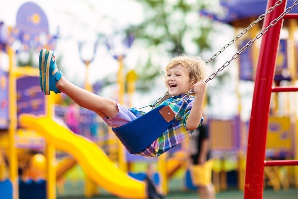 Ein lachendes, schaukelndes Kind auf einem bunten Spielplatz.