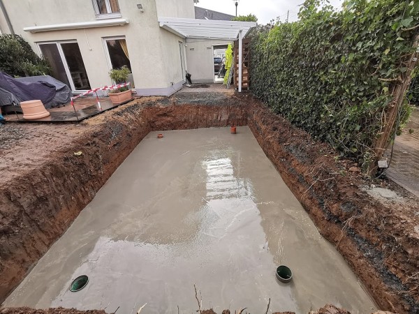 Ein umgegrabener Garten, am rechten Rand ist eine rechteckig ausgegrabene Grube, die mit Beton halb aufgegossen wurde.